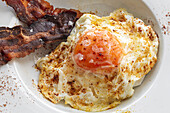 Overhead view of tasty eggs with fried bacon strips on plate