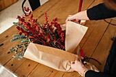 From above of crop unrecognizable female florist standing at wooden table arranging Christmas bouquet in room