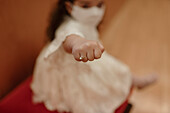 High angle soft focus of charming little girl in white dress and protective mask outstretching hand with elegant ring with pearl on finger