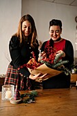 Fröhliche Freundinnen stehen am Tisch mit Kerzen und basteln kreative Weihnachtssträuße für die Weihnachtsfeier