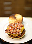 High angle of appetizing juicy hamburger with grilled bacon and cheese served on white plate placed on table