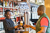 Cheerful black female barkeeper serving glass of refreshing beer for male client in bar