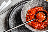 From above red fresh trout fish caviar served in a bowl on concrete table background