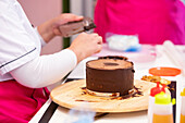 Crop unrecognizable person making biscuit cake with chocolate on wooden stand in bakery