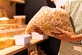 Soft focus of unrecognizable female vendor in striped apron carrying plastic bag of farfalle pasta during work in grocery store