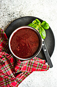 Beetroot cream soup served in the black ceramic bowl with fresh basil herb