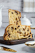 Rustic traditional Christmas panettone cake with raisins sliced on wooden board among luxurious breakfast tableware