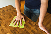 Cropped unrecognizable male wearing casual navy blue polo shirt wiping wooden dining table with yellow cloth