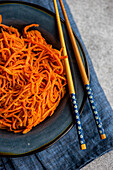 From above traditional spicy asian carrot salad served on ceramic plate and chopsticks on concrete background