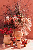 Composition of clay pots with blooming roses gypsophilia flowers and decorative grass at sunlight near red wall