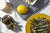 From above of traditional Spanish fried boquerones served on plates with lemons and bowl of white gazpacho soup placed on table with glass of beer in restaurant