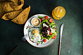 Traditionelles Mittagessen mit frischem Gemüsesalat, Spiegelei und Würstchen, serviert auf einem grünen Betontisch mit einem Glas frisch gepressten Orangensaft