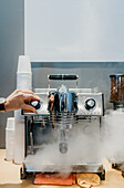 Crop anonymous barista using milk frother while cleaning coffee machine in cafeteria during work in daytime