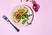 Tasty omelette on plate against fresh parsley sprigs and red onion with garlic cloves on pink background