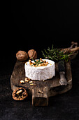 Delicious gourmet Camembert cheese garnished with walnuts and fresh rosemary served on rustic wooden board