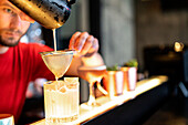 Focused bartender pouring cold refreshing cocktail through strainer in glass placed on counter in bar