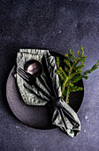 From above dark mood cutlery set with green napkin and modern metal cutlery on concrete table