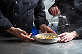 Crop chefs in black uniform removing dome lid from tasty dish on table while working in restaurant kitchen