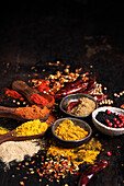 Assorted aromatic colorful spices in bowls and wooden spoons arranged on dark table with scattered condiments