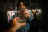 Soft focus of female barkeeper clinking glasses with splashing alcoholic drinks with crop anonymous man while standing in bar during work