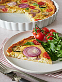 High angle of tasty vegetable quiche served on plate with ripe cherry tomatoes and fresh basil spinach during lunch at home