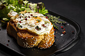 Fried egg on brioche served on tray with fresh lettuce for appetizing breakfast on black background