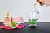 Crop unrecognizable person pouring milk from ceramic jug into glass cup placed near bowl and bamboo chasen