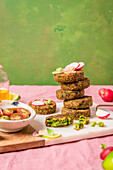 Vegan fritters stack served on cutting board near bowl of cherry tomatoes against green background