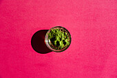 Top view of glass bowl with dried matcha tea on round bright on black pink background