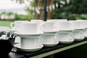 Stapel weißer Keramiktassen mit Untertassen auf dem Tresen in der Nähe einer Schale mit Mini-Kaffeesahne in einem Straßencafé