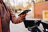 Selective focus of crop anonymous female using application on smartphone and scanning code of electric scooter on city street