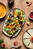 Top view of pumpkin salad with lettuce and spinach garnished with walnuts and pomegranate seeds and served on plate near soup and berry sauce