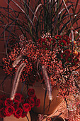 Komposition aus Tontöpfen mit blühenden Rosen, Schleierkraut und dekorativem Gras im Sonnenlicht an einer roten Wand