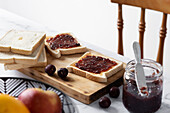 High angle of appetizing crispy toasts with cherry jam served on wooden chopping board near fresh ripe berries on table