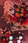 Von oben eleganter Strauß frischer üppiger roter Rosen und Lilien mit Zweigen roter Beeren in der Nähe von Stoff und Kerzen auf dem Boden