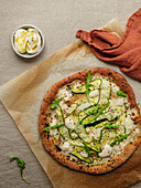 Top view of tasty pizza with squash slices and condiments with fresh arugula leaves on parchment paper on beige background