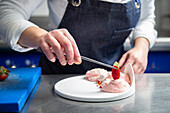 Anonymous woman in apron using tweezers to put slice of fresh strawberry on top of whipped cream while cooking dessert in kitchen of contemporary restaurant