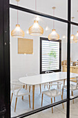 Through glass of white chairs and table placed near counter and window in modern light cafeteria with hanging glowing lamps