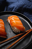 Top view composition of delicious fresh sushi and bamboo chopsticks served on black platter on checkered cloth