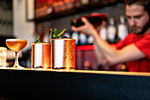 Moscow mule cocktail in copper mugs served on counter in bar on background of blurred barman with shaker