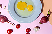Draufsicht auf rohe Eier auf einem Teller vor Eierschalen und frischen Petersilienzweigen auf zweifarbigem Hintergrund