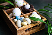 From above spring Easter wooden box with colored eggs and nest surrounded by italian Ruscus plant
