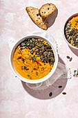 Top view of white ceramic bowls with delicious healthy pumpkin cream soup with seeds and rosemary placed on table in kitchen