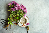 Tasse mit Milchkaffee und herbstlichen lila Chrysanthemenblüten auf Betontisch