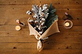 From above of festive Christmas bouquet with branches of cotton and fir placed on wooden table with candles in room