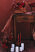 Wooden old fashioned table decorated with fabric and vases of red flowers near burning candles in studio