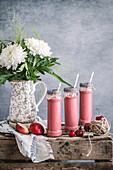 Erfrischender Milchshake mit Nektarinen und Kirsche, serviert in Gläsern auf einem Holztisch mit Blumen