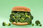 Hälften eines Burgerbrötchens mit einem Bündel roher Brokkoli auf grünem Hintergrund während eines gesunden Mittagessens