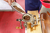 Unbekannter Barista gießt Kaffeebohnen aus einer Schaufel in eine manuelle Kaffeemühle vor einem unscharfen Hintergrund