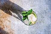 Glass of lemon water with mint on concrete background in sunny day with shadows